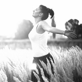 Eine Frau läuft auf einer Wiese mit offenen Armen und geschlossenen Augen